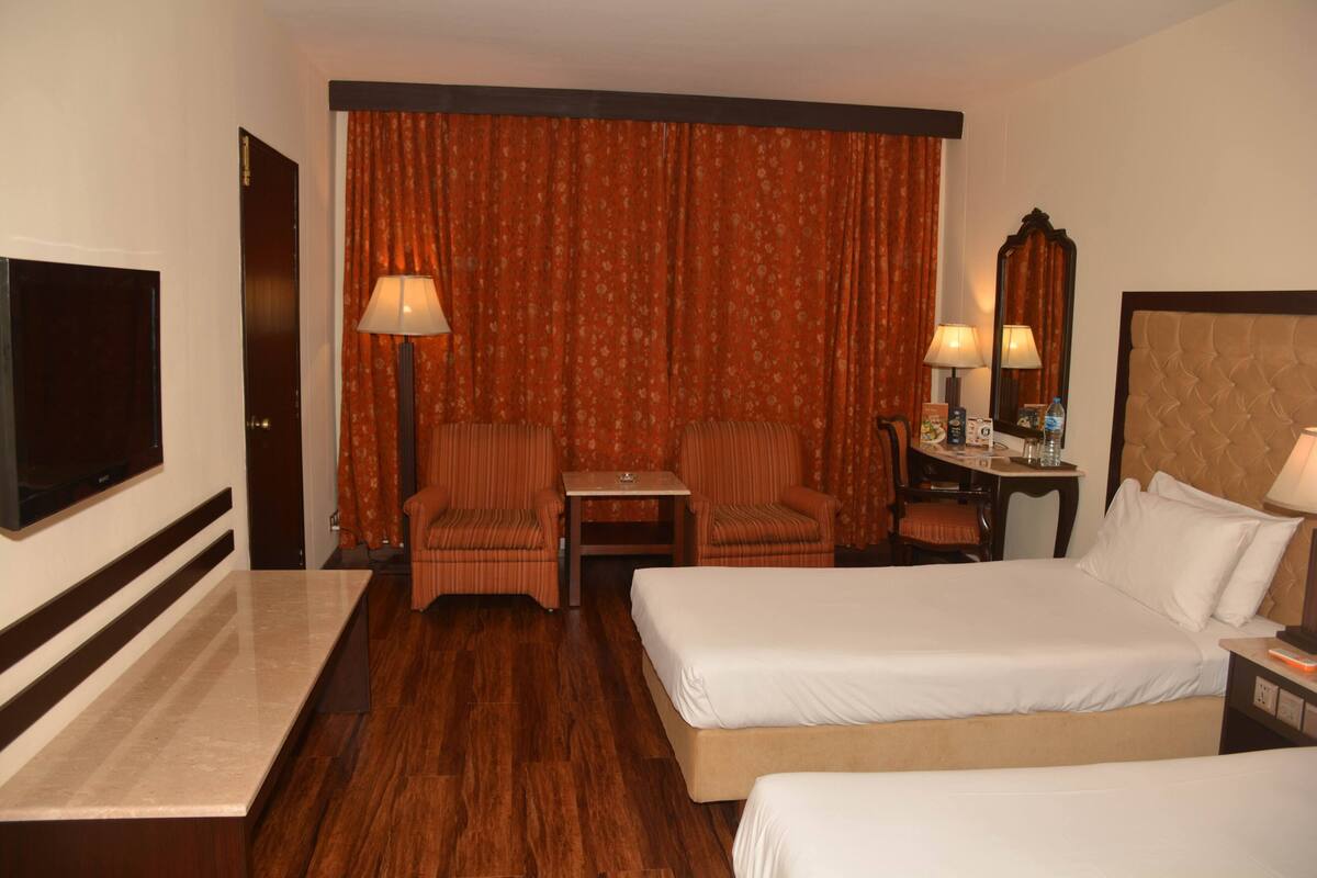 A hotel room with a bed, two chairs, a desk, a TV, and a large window with curtains.