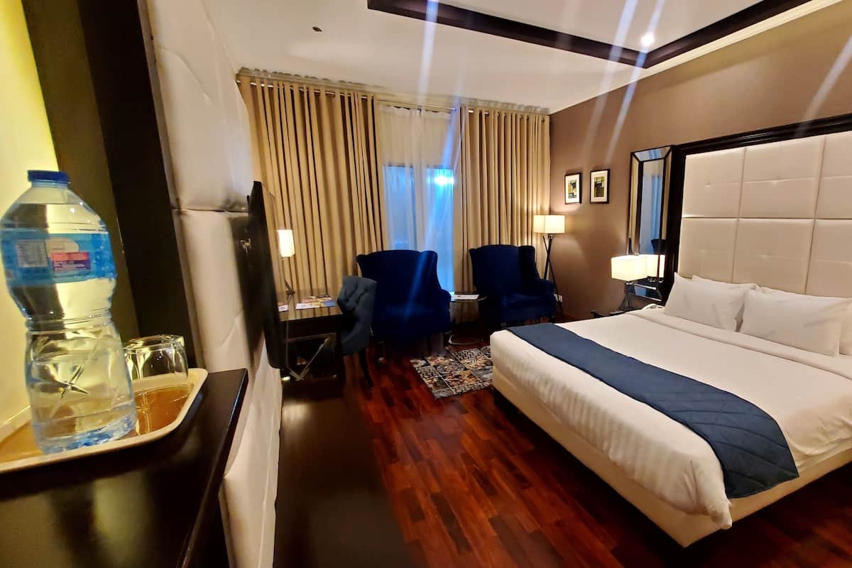 A hotel room with a large bed, two armchairs, a desk, a water bottle, and a mirror.