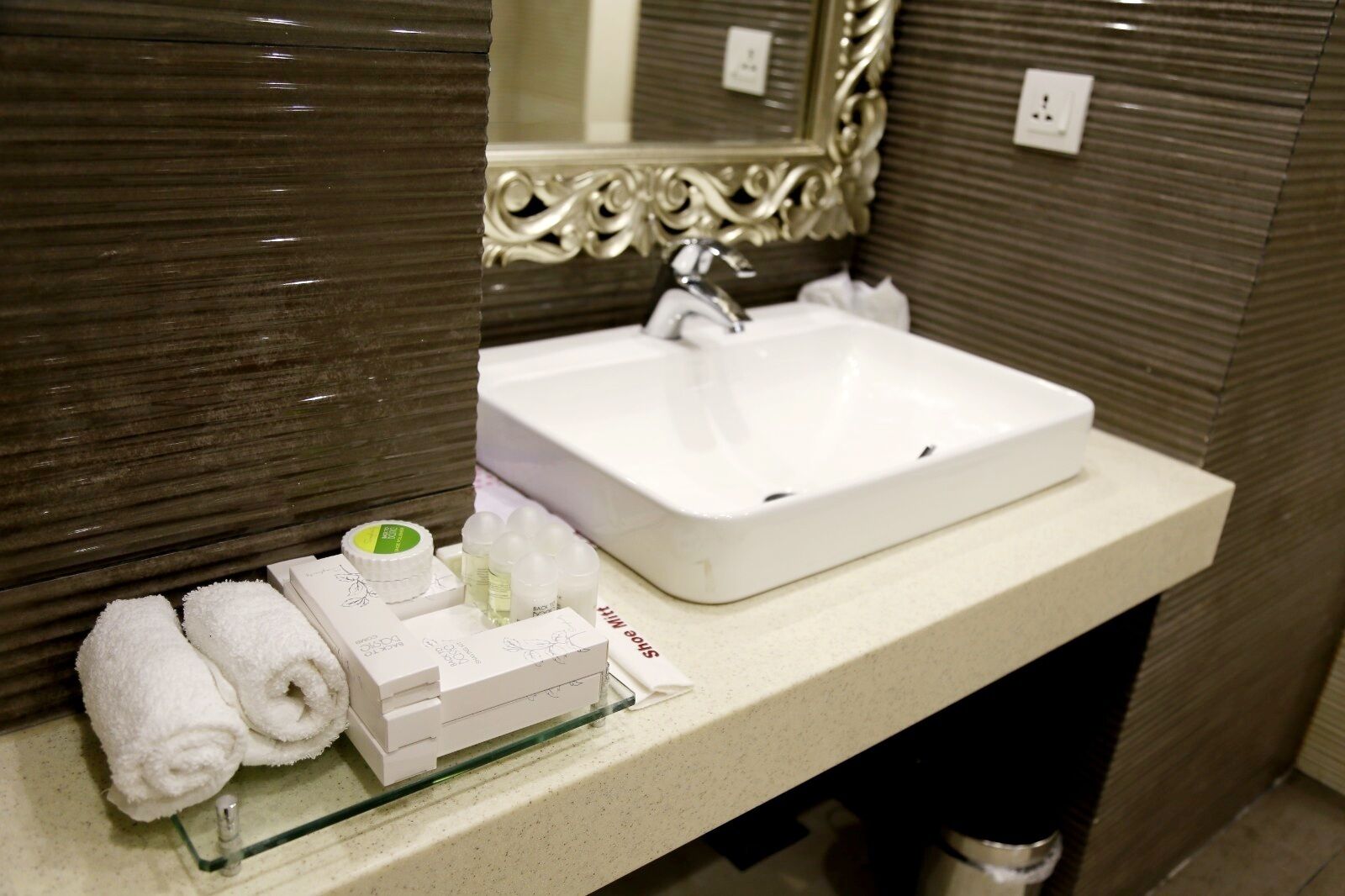Un baño con un lavamanos blanco, un espejo con marco decorativo y artículos de aseo en la encimera.