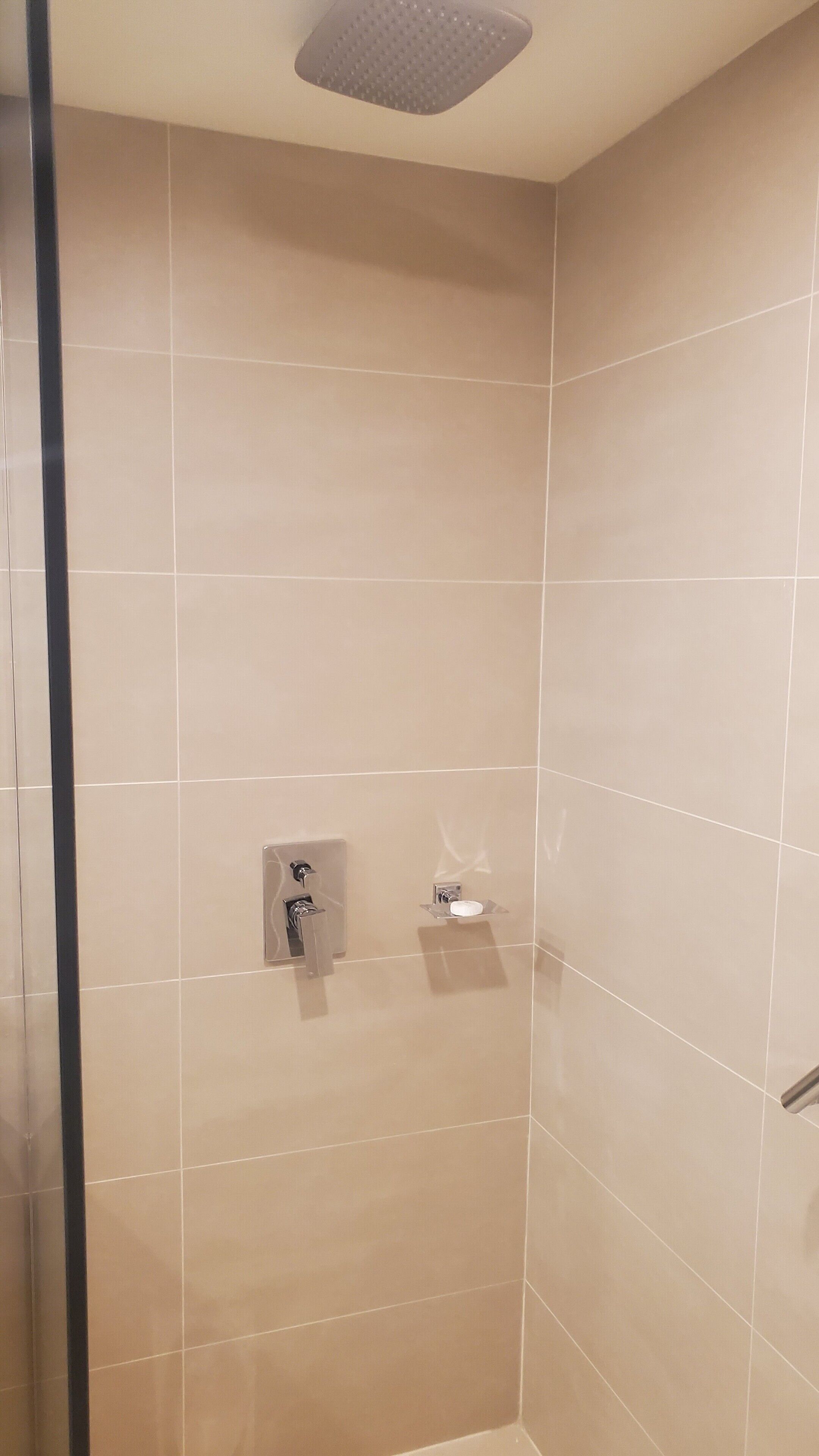Una ducha con azulejos color beige, un cabezal de ducha manual y un pequeño estante con un jabonera.
