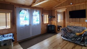A wooden cabin interior with a sofa, a television, and a fireplace.