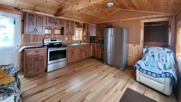 A wooden cabin interior with a kitchen, a dining area, and a sofa.