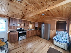 A wooden cabin interior with a kitchen, a dining area, and a sofa.
