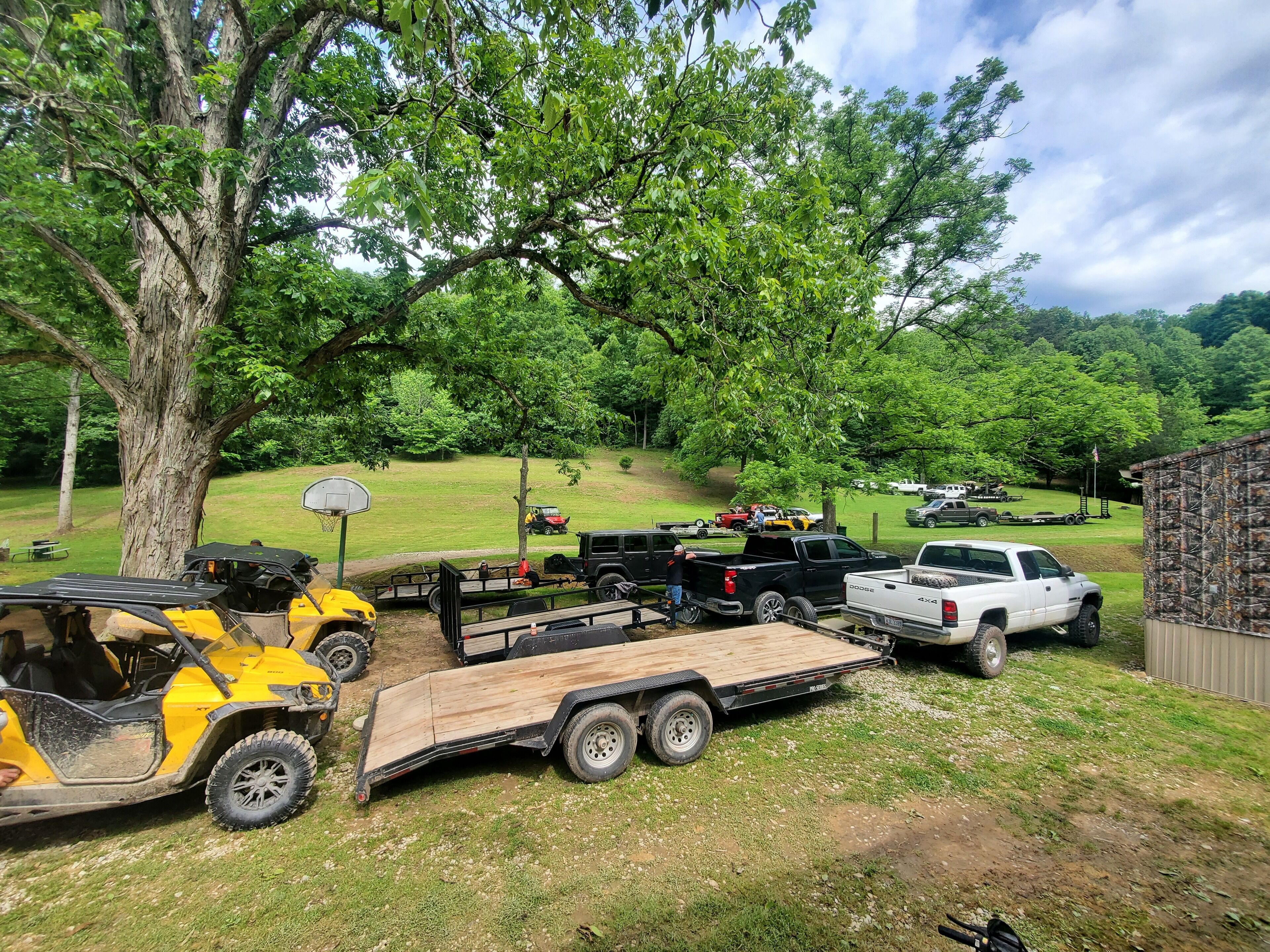 A parking area with various vehicles, including a yellow ATV, a black pickup truck, and a white pickup truck.