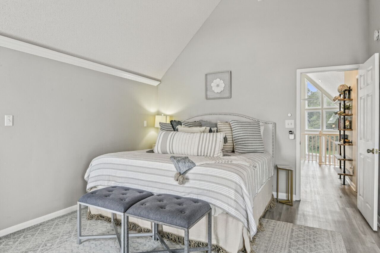 A bedroom with a bed, bedside table, lamp, and a view of the outside.