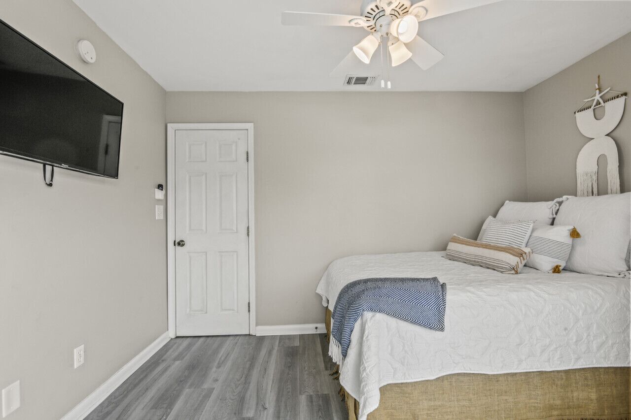 Une chambre à coucher avec un lit, un ventilateur de plafond, un téléviseur fixé au mur et une porte.