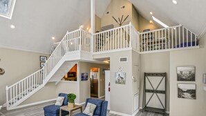 Un espacio habitable amplio con una escalera blanca que lleva a un altillo, un comedor y una cocina.