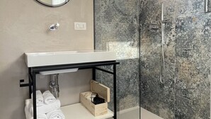 Een moderne badkamer met een wit wastafelmeubel, een spiegel, een zwart metalen plankje en een douchecabine met glazen wanden.