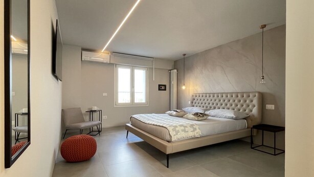 Een moderne slaapkamer met een groot bed, een stoel, een klein tafeltje en een rode poef.