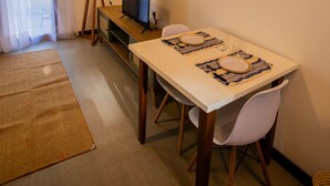 Una habitación acogedora con techo de madera, un televisor sobre un mueble, una mesa de comedor con sillas y una lámpara.