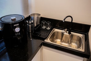 Uma cozinha com uma cafeteira preta, uma pia de aço inoxidável e uma bancada preta.