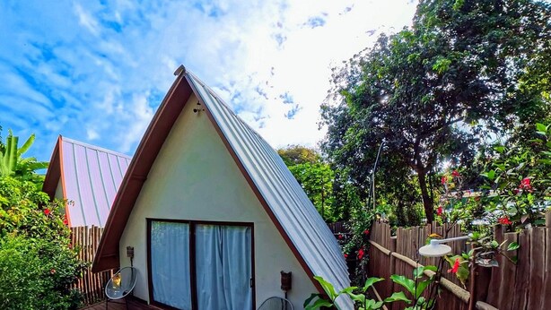 Una casa con techo inclinado, terraza de madera y jardín con diversas plantas.