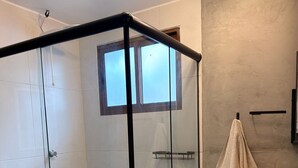 Un baño moderno con ducha compartimentada por vidrio, tocador de madera y perchero.