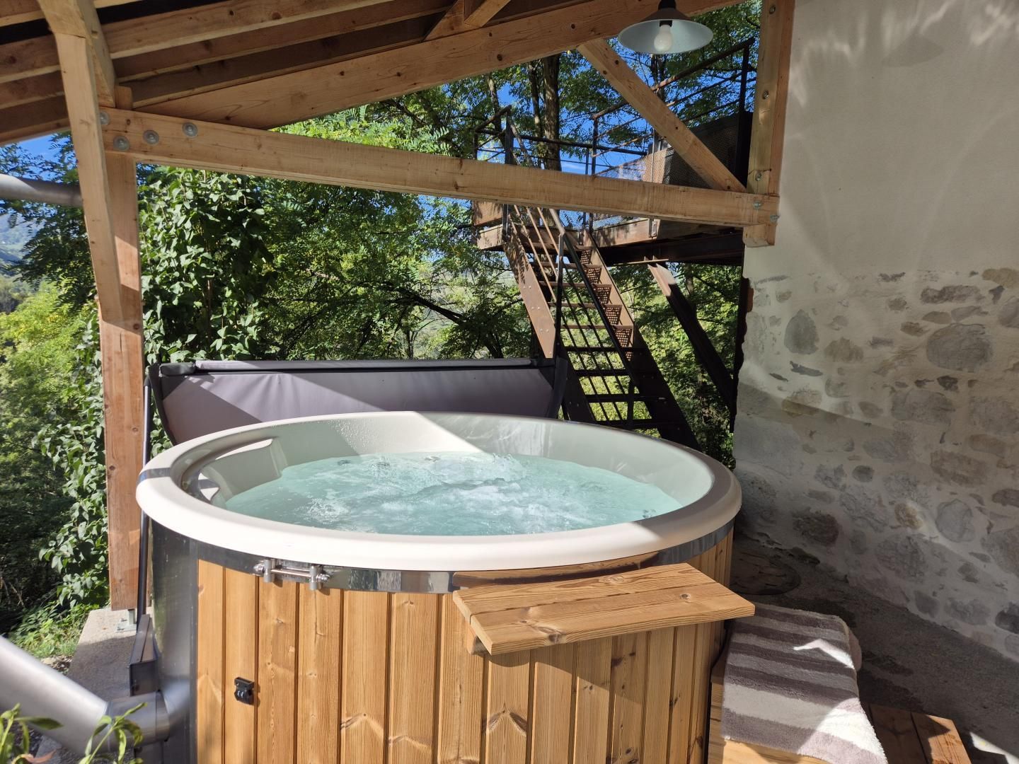 Een hottub onder een houten pergola, met een stenen muur op de achtergrond.