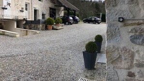 Un edificio de piedra con camino de grava, coches estacionados y plantas en macetas.