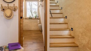 Una escalera con escalones de madera y una pared con textura. Un espejo cuelga de la pared, y se ve una mesita con un objeto morado.