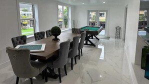 Una habitaci ón amplia con mesa de billar, un comedor con una mesa grande y sillas, y ventanas grandes que ofrecen vistas al exterior.