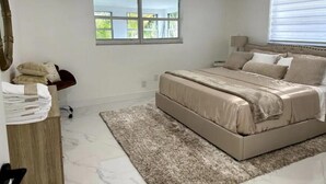 Un dormitorio con cama, ventilador de techo, ventana y mesita de noche con lámpara.