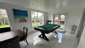 Una habitación moderna con mesa de billar, un sillón cómodo y ventanas amplias con vistas al exterior.
