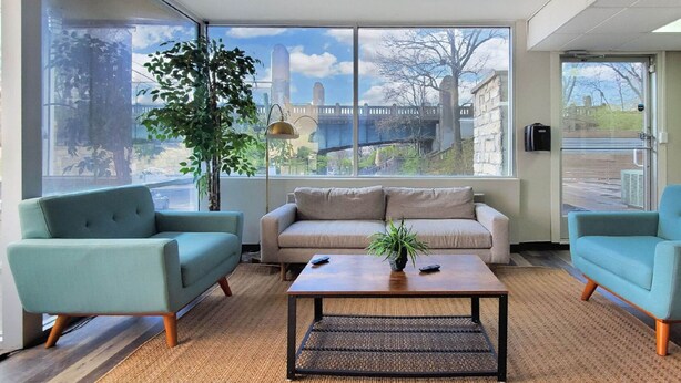 A room with a sofa, two armchairs, a coffee table, and a large window with a view of buildings and a bridge. - Sleepover | Cozy 1BD/1BA + Gym - Cincinnati (Cincinnati)