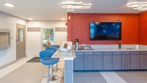 A modern kitchen with a TV, bar stools, and a red accent wall. - Sleepover | Cozy 1BD/1BA + Gym - Cincinnati (Cincinnati)