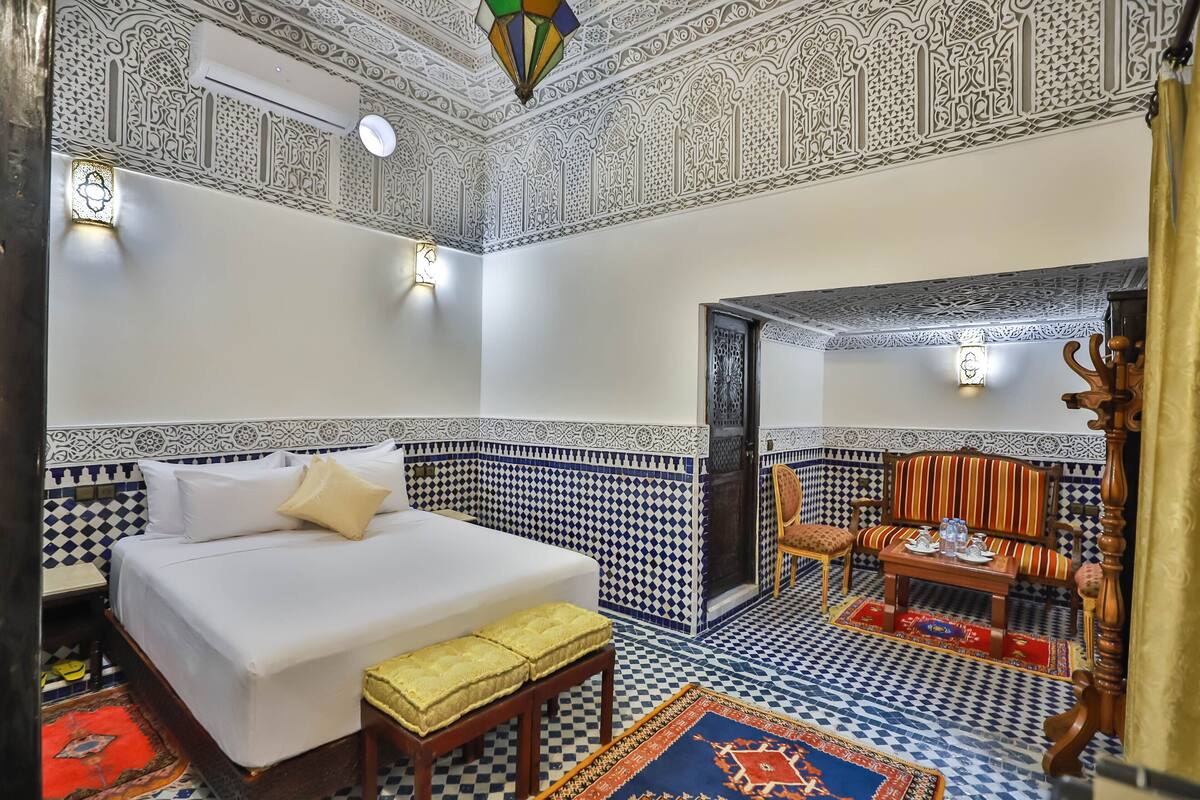A room with a bed, a sofa, a small table, and a patterned floor.