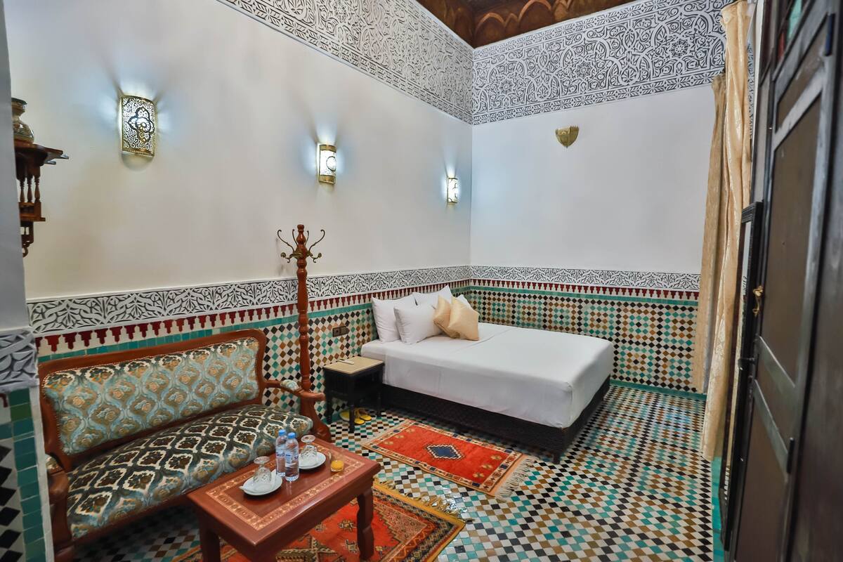 A room with a bed, a sofa, a small table, and a decorative wall with intricate patterns.