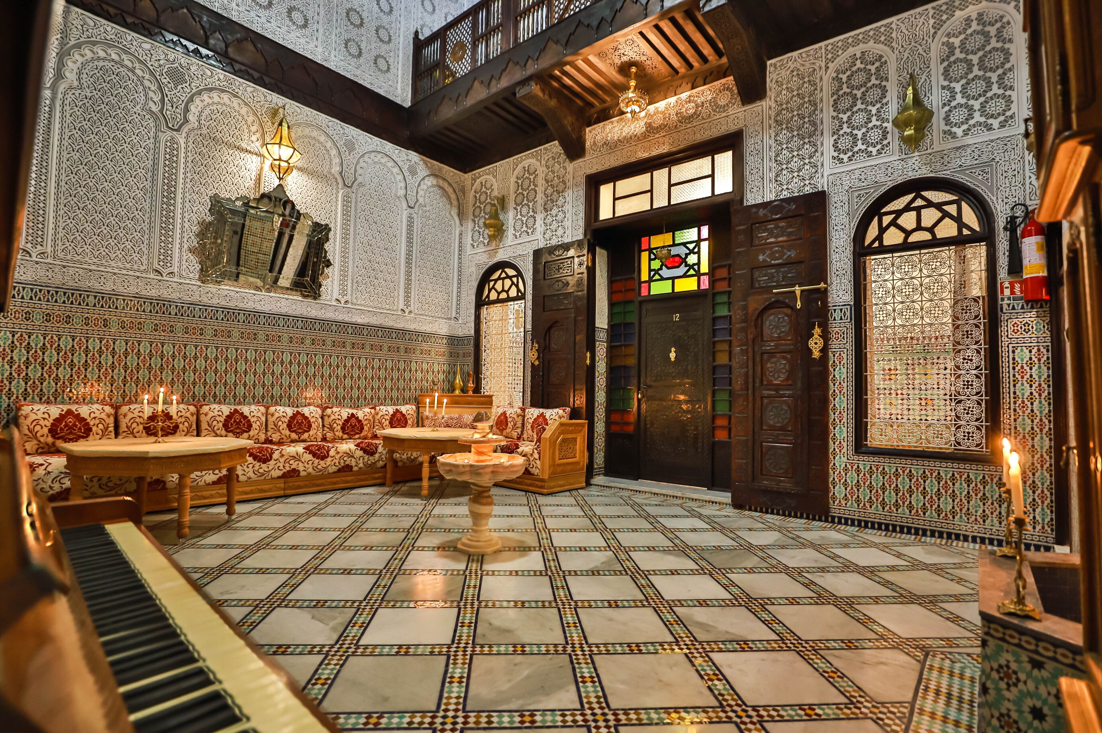 A room with intricate tile work, a piano, a sofa set, and a fountain.
