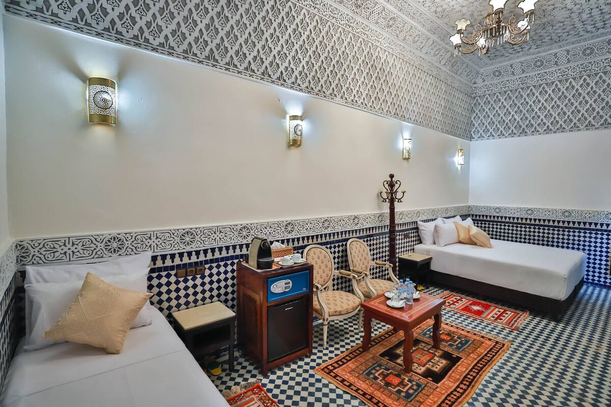 A room with patterned walls, a sofa, a small table, a chair, and a decorative ceiling light.