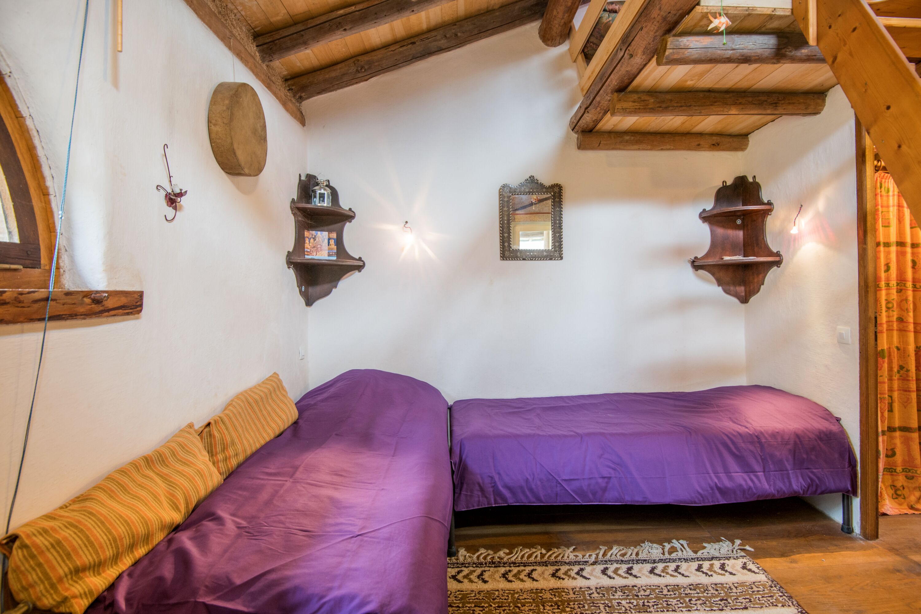 A room with two beds, wooden beams on the ceiling, a wall-mounted mirror, and a patterned rug.