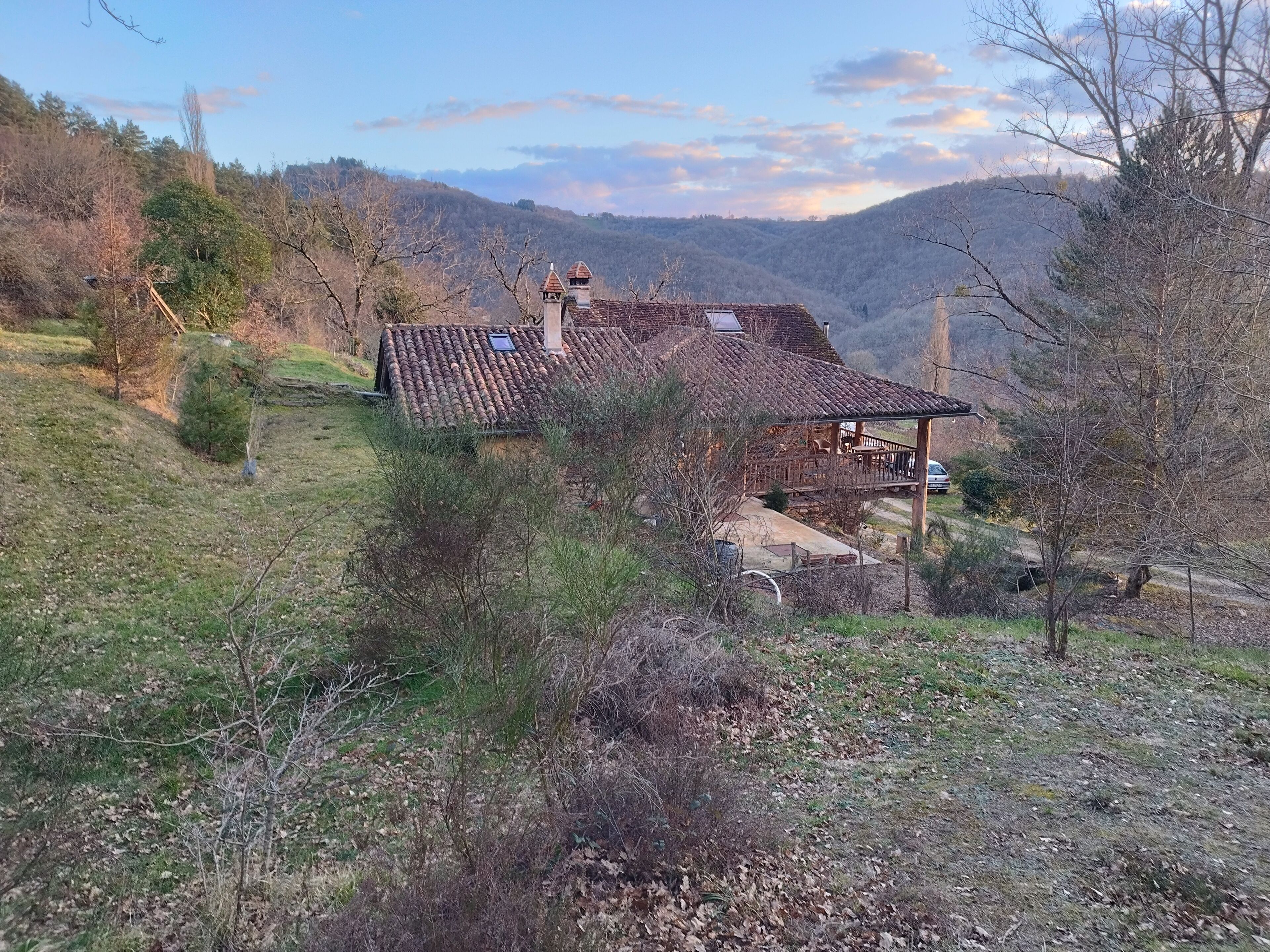 A rustic house with a tiled roof, surrounded by a hilly landscape.