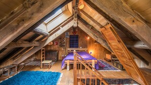 An attic bedroom with a wooden ceiling, a bed, a blue rug, and a staircase. - GiteleCun (Frayssinhes)