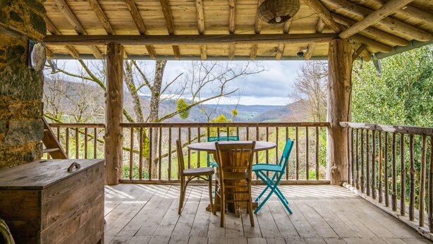 A wooden deck with a table and chairs, overlooking a mountainous landscape. - GiteleCun (Frayssinhes)