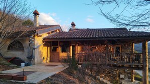 A rustic house with a tiled roof, a wooden porch, and a stone chimney. - GiteleCun (Frayssinhes)