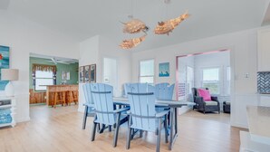 A spacious dining area with a wooden table and blue chairs, a bar area with stools, and a seating area with a wicker chair and cushions. - 5951- South Of Stars - South Nags Head Escape w/ Pool & Hot Tub (Nags Head)