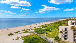 En fastighet som ligger direkt vid stranden, med en sandstrand, en klarblå himmel och utsikt över havet.