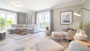 A spacious living room with a large sofa, a coffee table, and a side table with decorative vases. - Wattblick. Reet. Sauna. - Hideaways (Sylt)