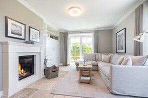 A living room with a fireplace, a sofa, a coffee table, and a large window. - Wattblick. Reet. Sauna. - Hideaways (Sylt)