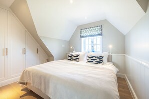 A bedroom with a large bed, a window with a patterned curtain, and a staircase leading to an upper level. - Wattblick. Reet. Sauna. - Wattgeflüster (Sylt)