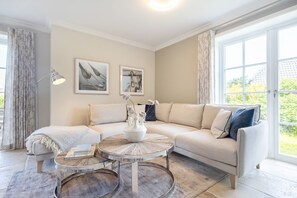 Una sala de estar moderna con un sofá color beige, dos mesitas auxiliares y un ventanal con cortinas.