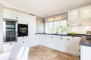 A modern kitchen with white cabinetry, a black countertop, and a large window with a view of greenery. - Wattblick. Reet. Sauna. - Wattgeflüster (Sylt)