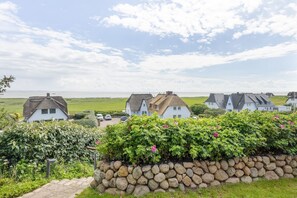 A coastal village with traditional houses, a stone wall, and a view of the sea. - Wattblick. Reet. Sauna. - Wattgeflüster (Sylt)