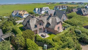 Un village côtier doté de maisons traditionnelles aux toits de chaume, d’une allée pavée et offrant une vue dégagée sur la mer.