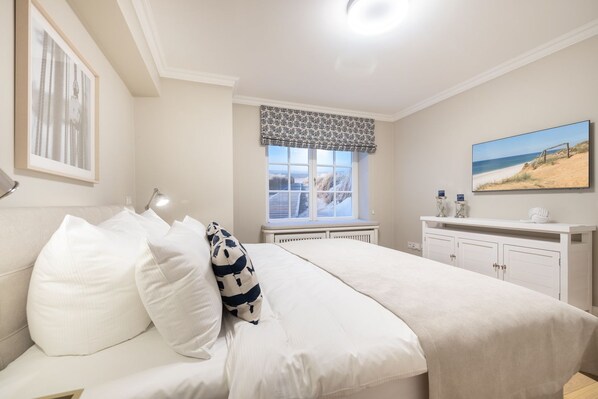 Un dormitorio con una cama, una ventana con vistas, un aparador y un cuadro en la pared.