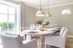 A dining area with a round table set for six, light-colored chairs, and pendant lighting. - Wattblick. Reet. Sauna. - Wattgeflüster (Sylt)