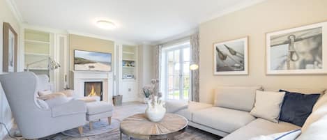 A spacious living room with a fireplace, a large sofa, a coffee table, and a bookshelf.