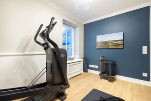 Un gimnasio en casa con una bicicleta estática, una cinta de correr y una colchoneta de yoga sobre piso de madera.