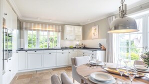 Une cuisine moderne avec des meubles blancs, un coin repas doté d’une table ronde pour quatre personnes et de grandes fenêtres laissant entrer la lumière naturelle.