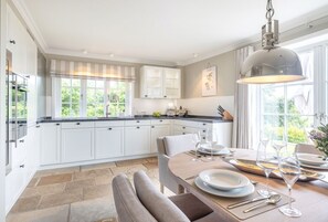 A modern kitchen with white cabinetry, a dining area with a round table set for four, and large windows providing natural light.