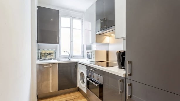 A compact kitchen with a washing machine, oven, microwave, and a window providing natural light. - Splendid Apartment in the Very Center Paris / Great for Olympic Games 2024 (Paris)